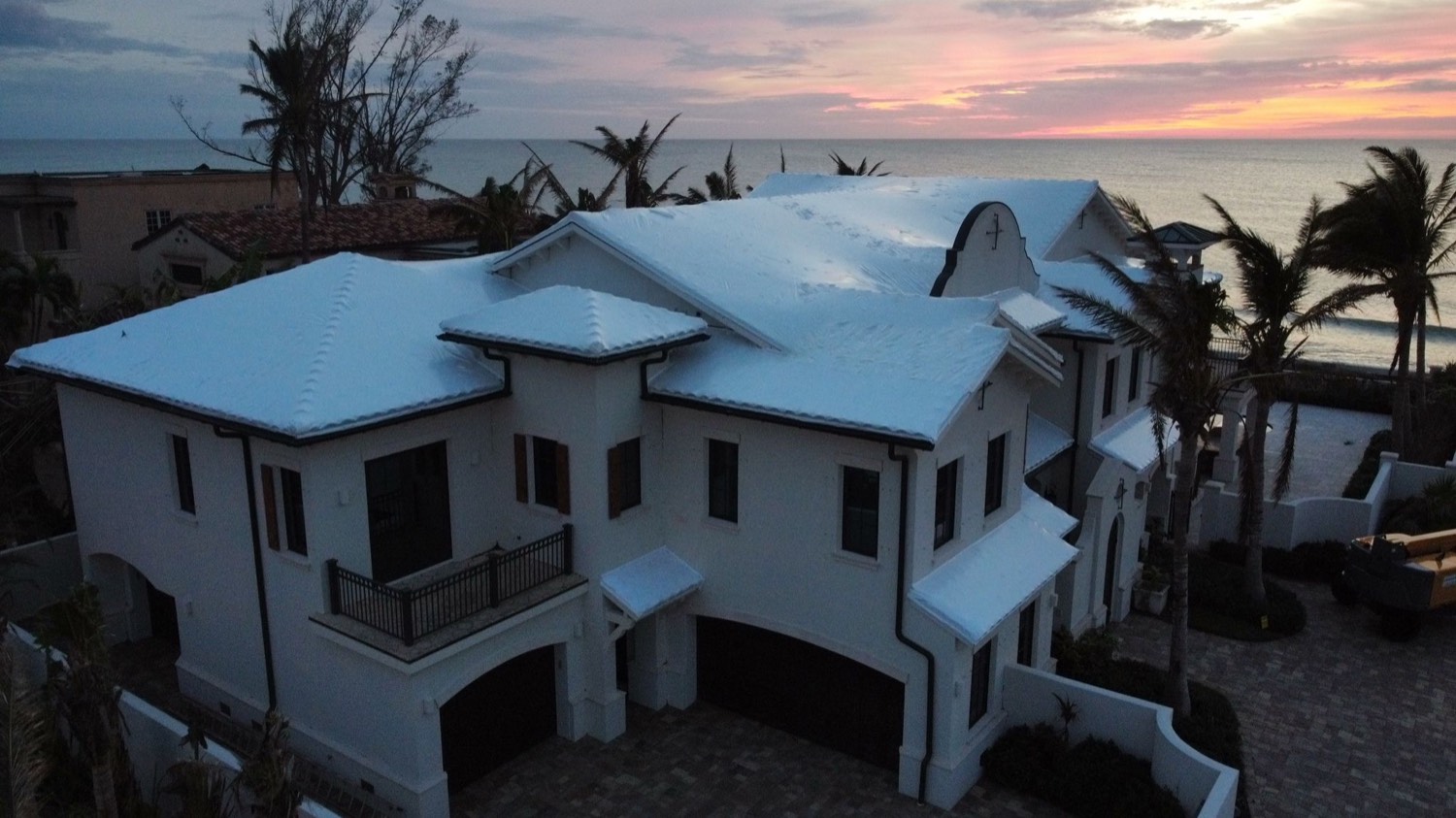 Luxury coastal home with every roof plane sealed under a white RoofWrap membrane at sunset