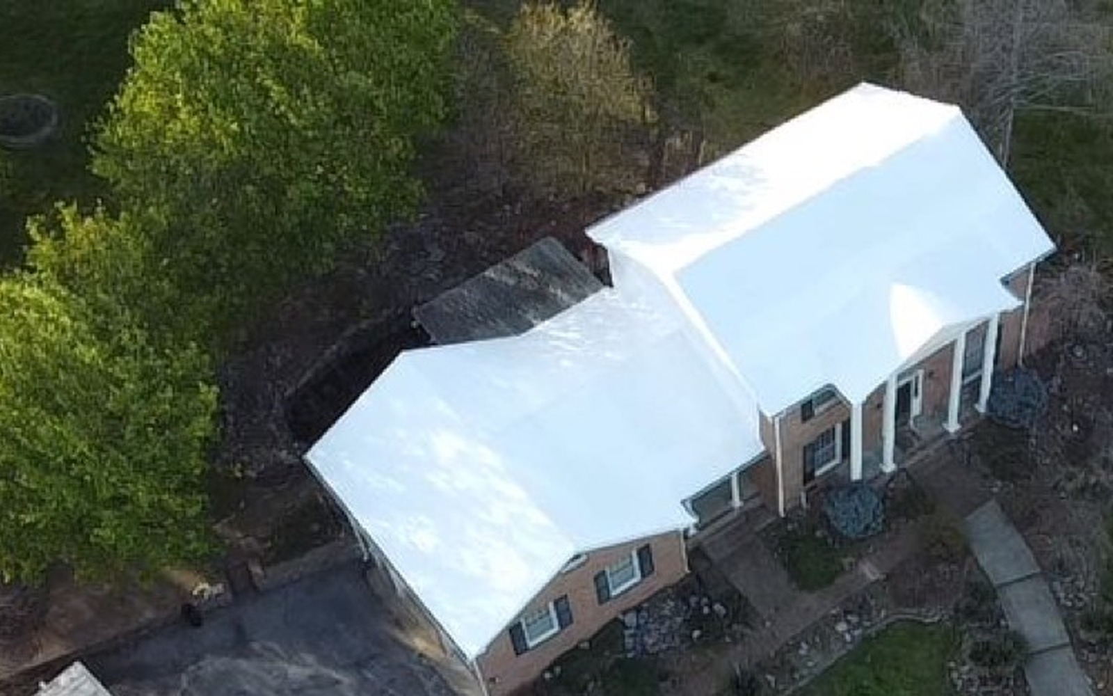The same brick colonial home with its fire-damaged wing sealed under a white RoofWrap membrane