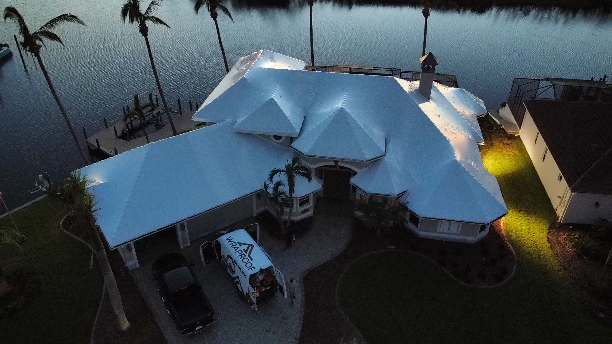 The same waterfront home sealed under a clean white RoofWrap membrane at dusk